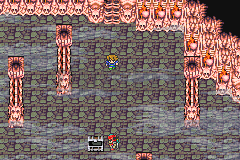Une salle du château sous sa vraie forme : sol dallé entre les piliers de chair, un coffre en bas (version GBA)